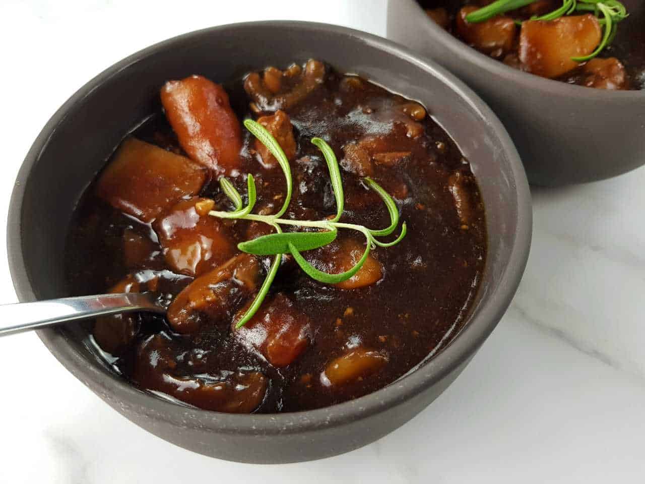 Beef and ale stew in gray bowls with spoons on a marble table.