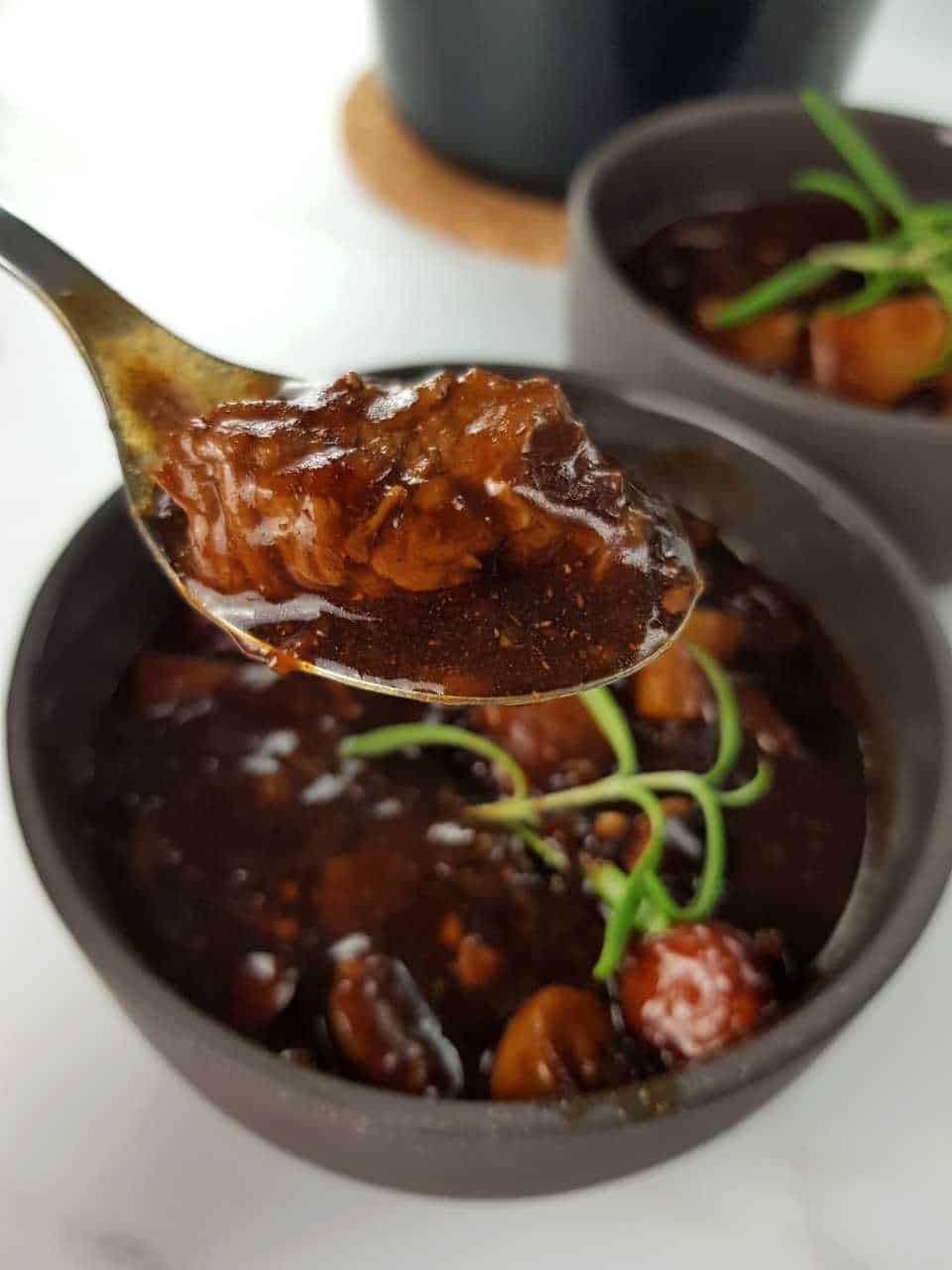 Beef and ale stew in a gar bowl. A fork is lifting some of the stew out of the bowl.