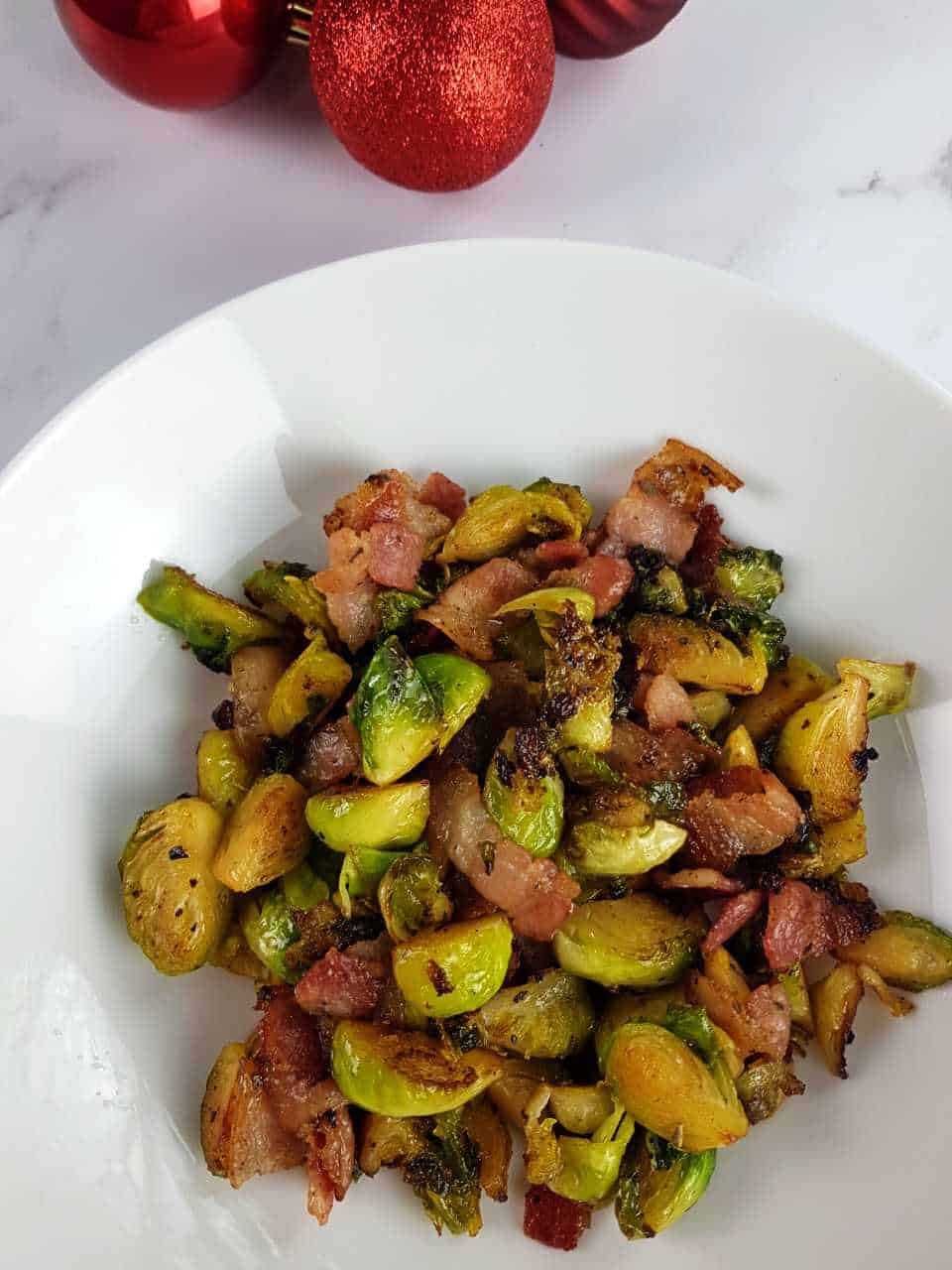 Brussels sprouts with bacon and maple syrup on a white plate on a marble table.