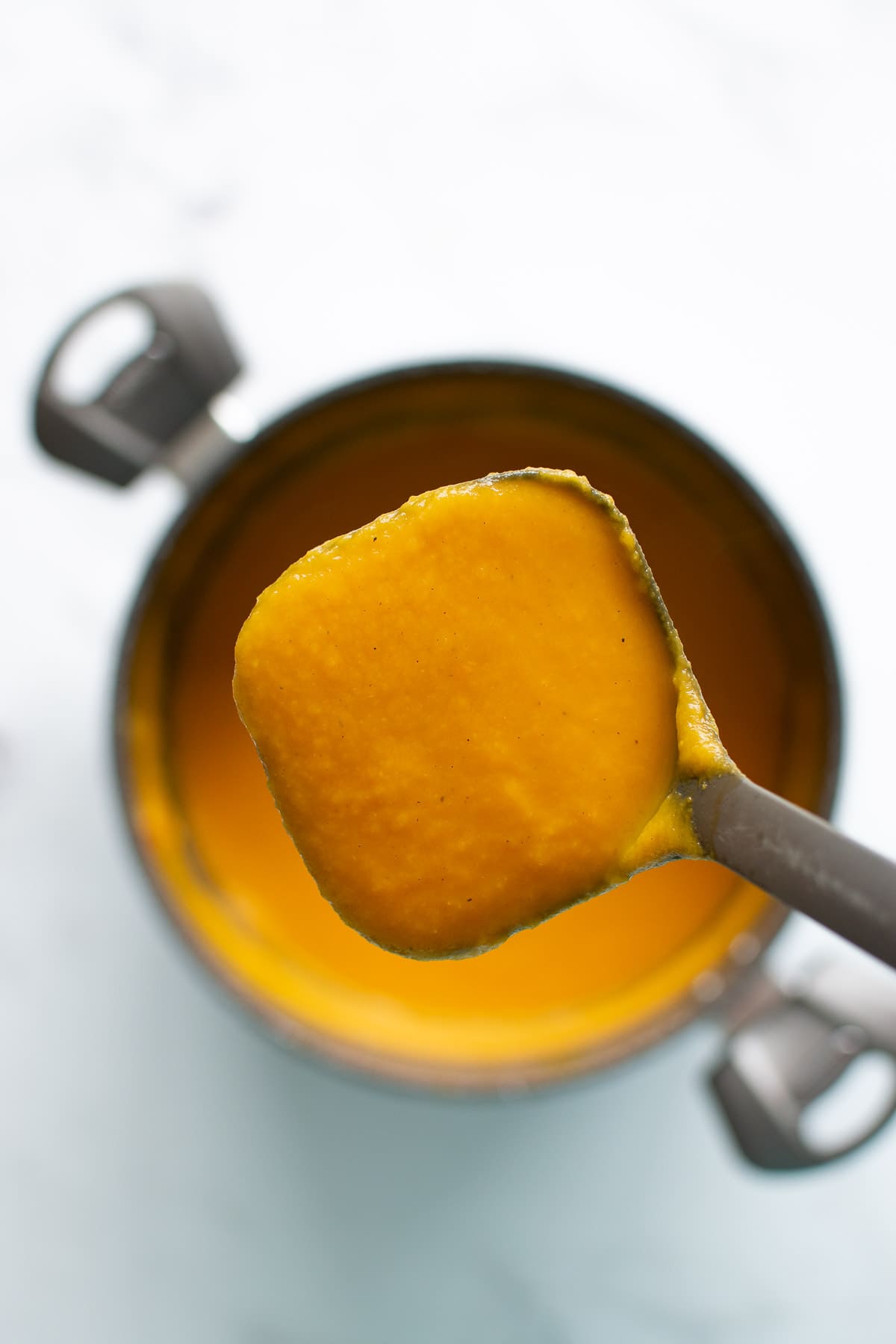 Close up of a ladle filled with carrot soup