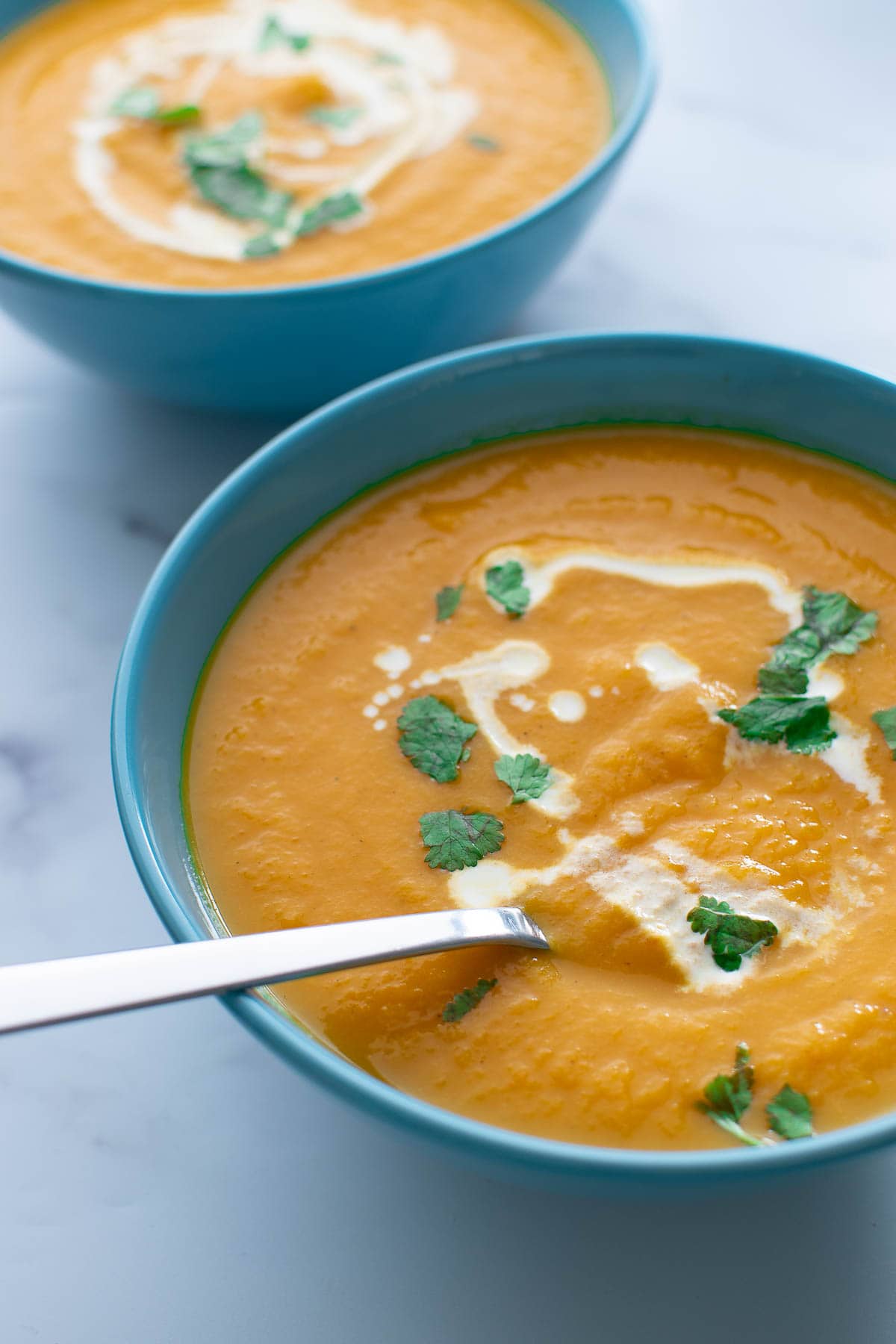 Two bowls of carrot and ginger soup with spoons.