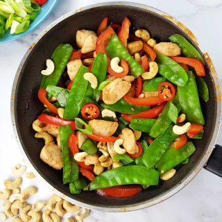 Cashew chicken stir fry in a frying pan on a marble table.