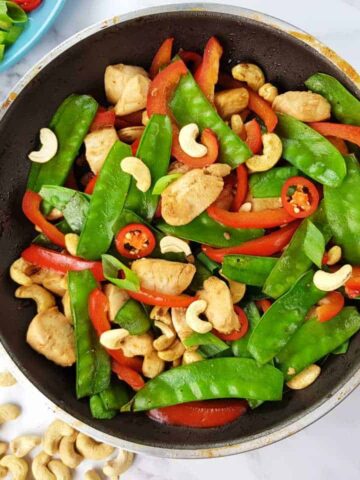 Cashew chicken stir fry in a frying pan on a marble table.