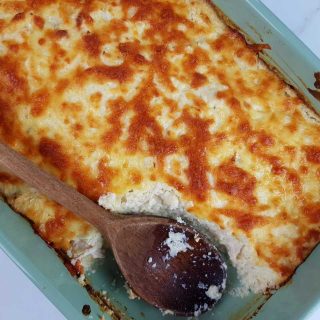 Cauliflower rice and chicken casserole in a blue casserole dish with a wooden spoon.