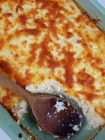 Cauliflower rice and chicken casserole in a blue casserole dish with a wooden spoon.