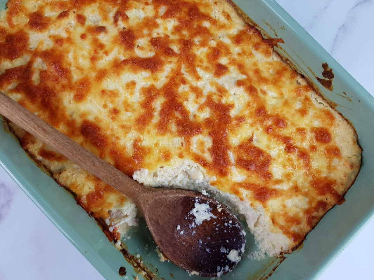 Cauliflower rice and chicken casserole in a blue casserole dish with a wooden spoon.