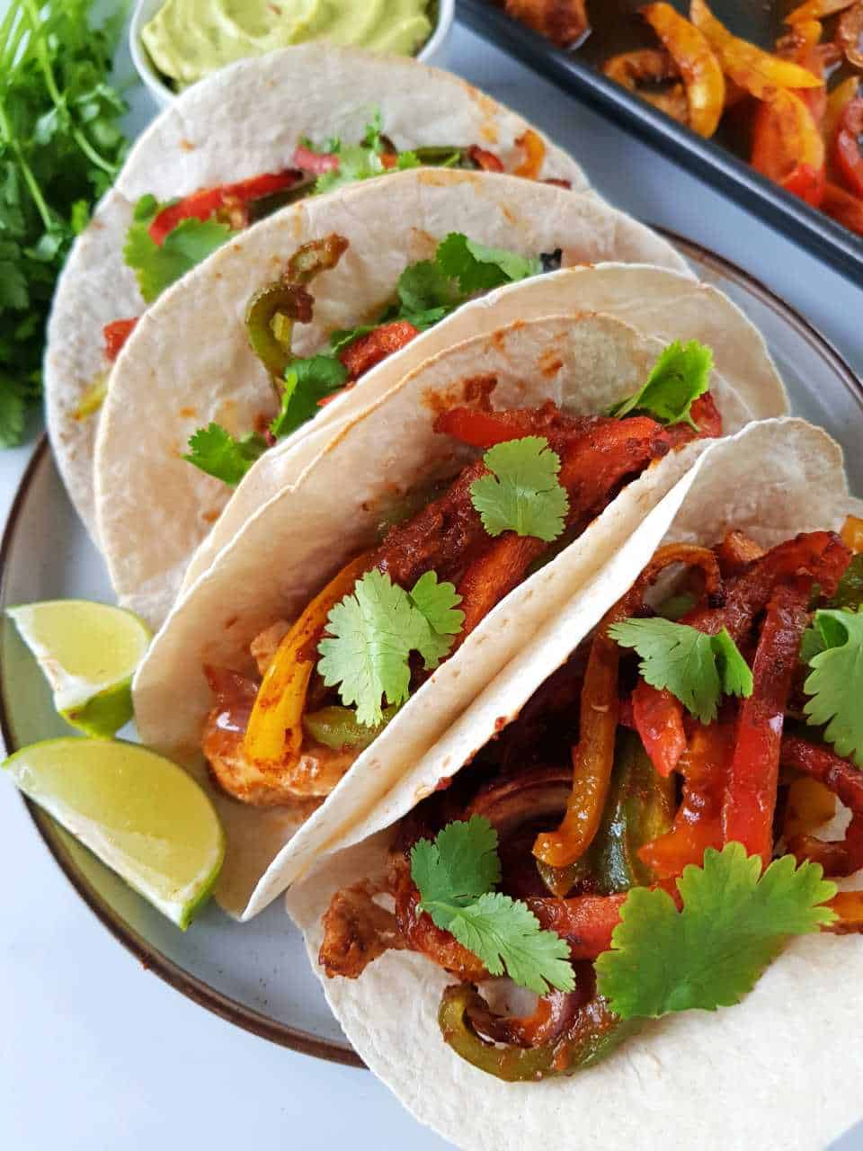 Fajitas topped with cilantro on a plate with lemon wedges on the side.