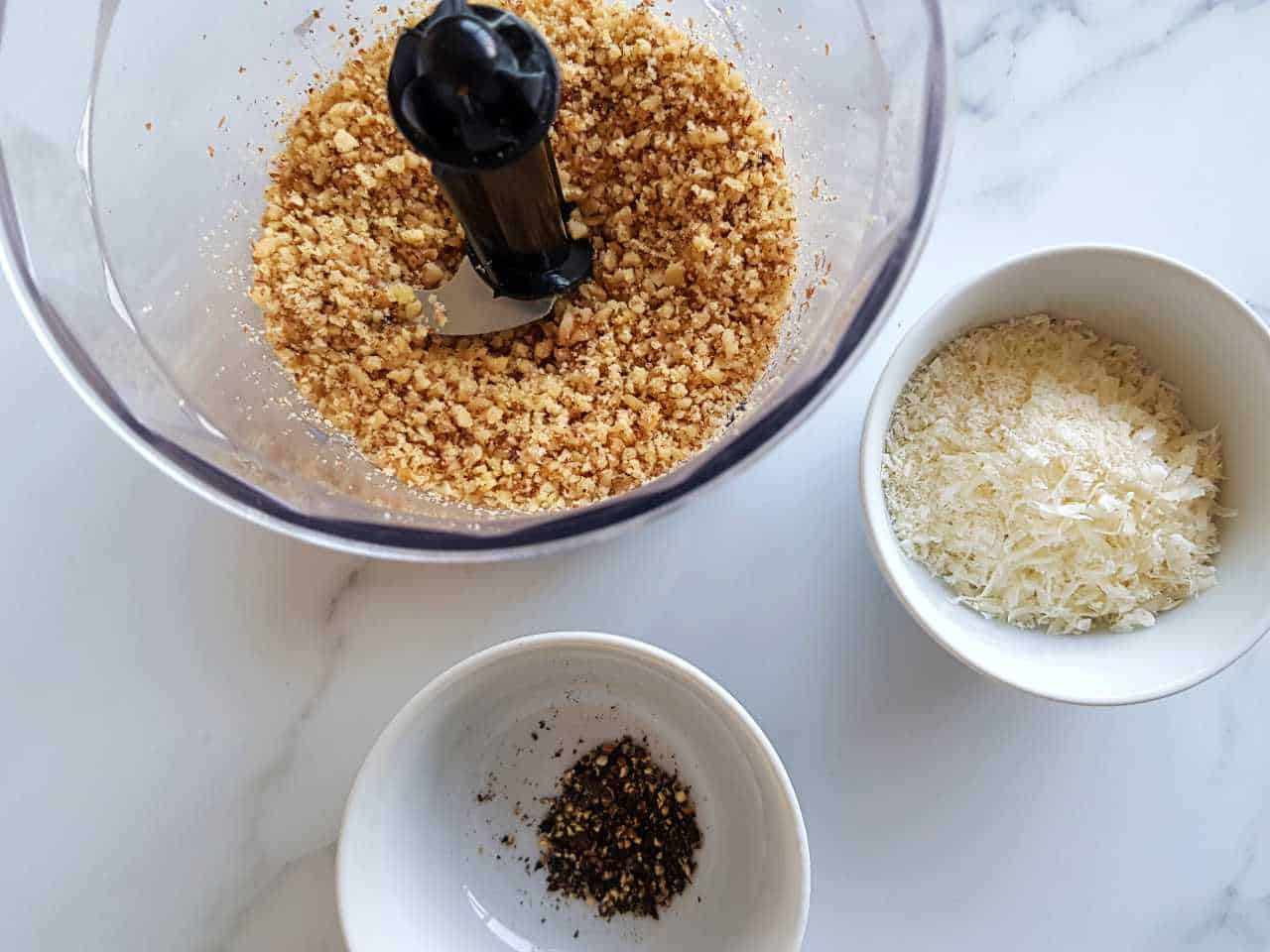 Ingredients for walnut crusted chicken in white bowls on a marble table.