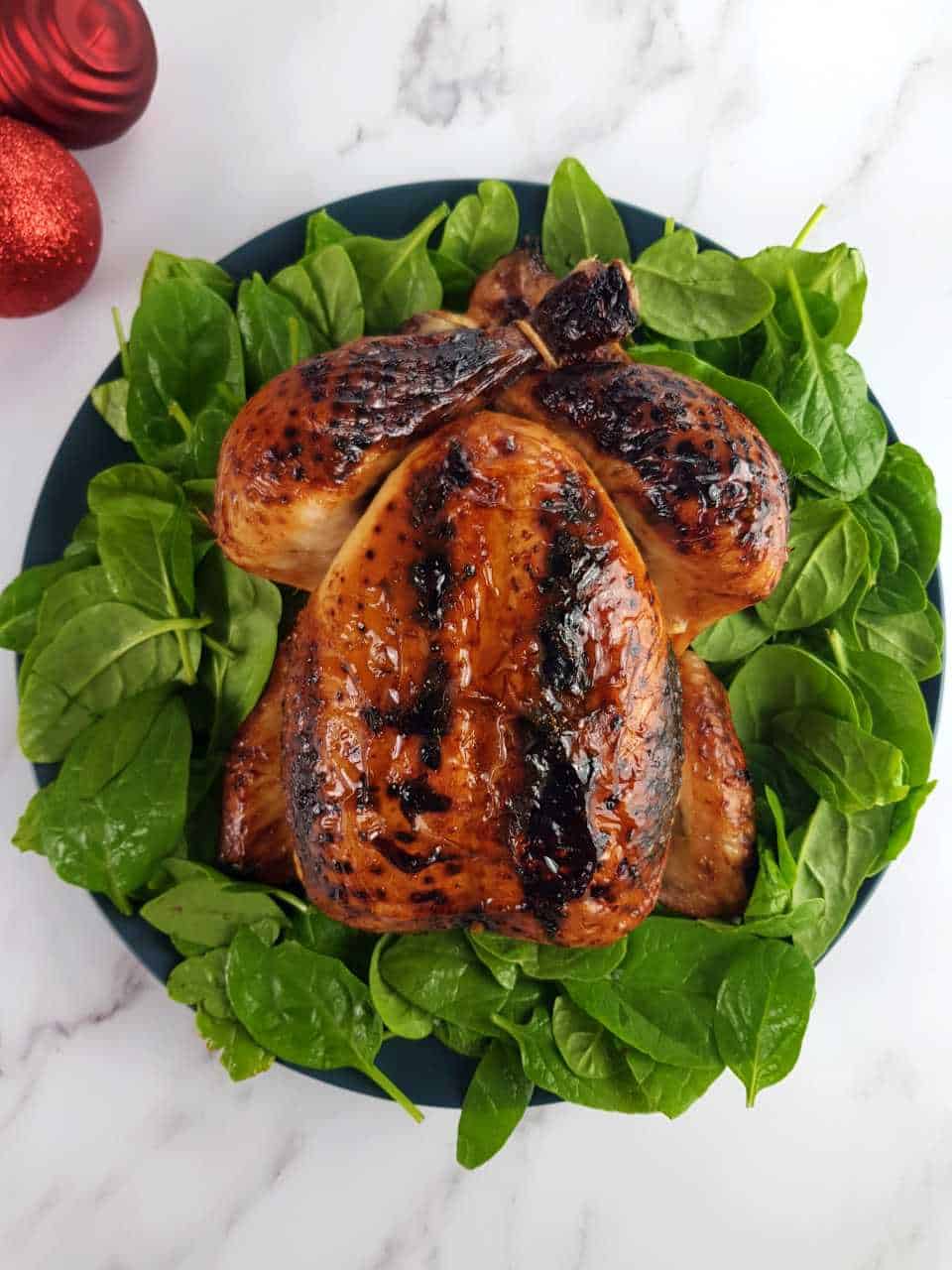 Roast chicken in honey on a bed of spinach on a marble table.