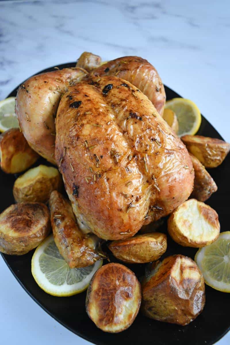 Roast chicken on a plate with lemon slices and potatoes.