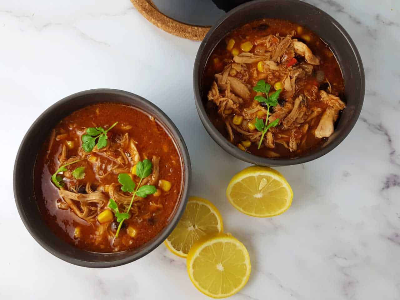 Slow cooker chicken taco soup in bowls on a marble table with lemon slices in front.