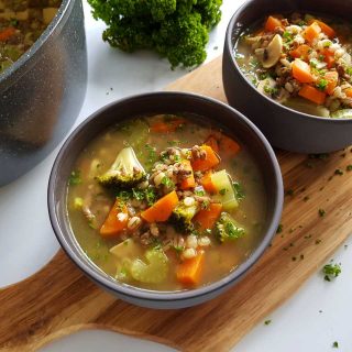 Barley soup with ground beef in bowls on a wooden chopping board.