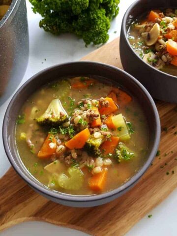 Barley soup with ground beef in bowls on a wooden chopping board.