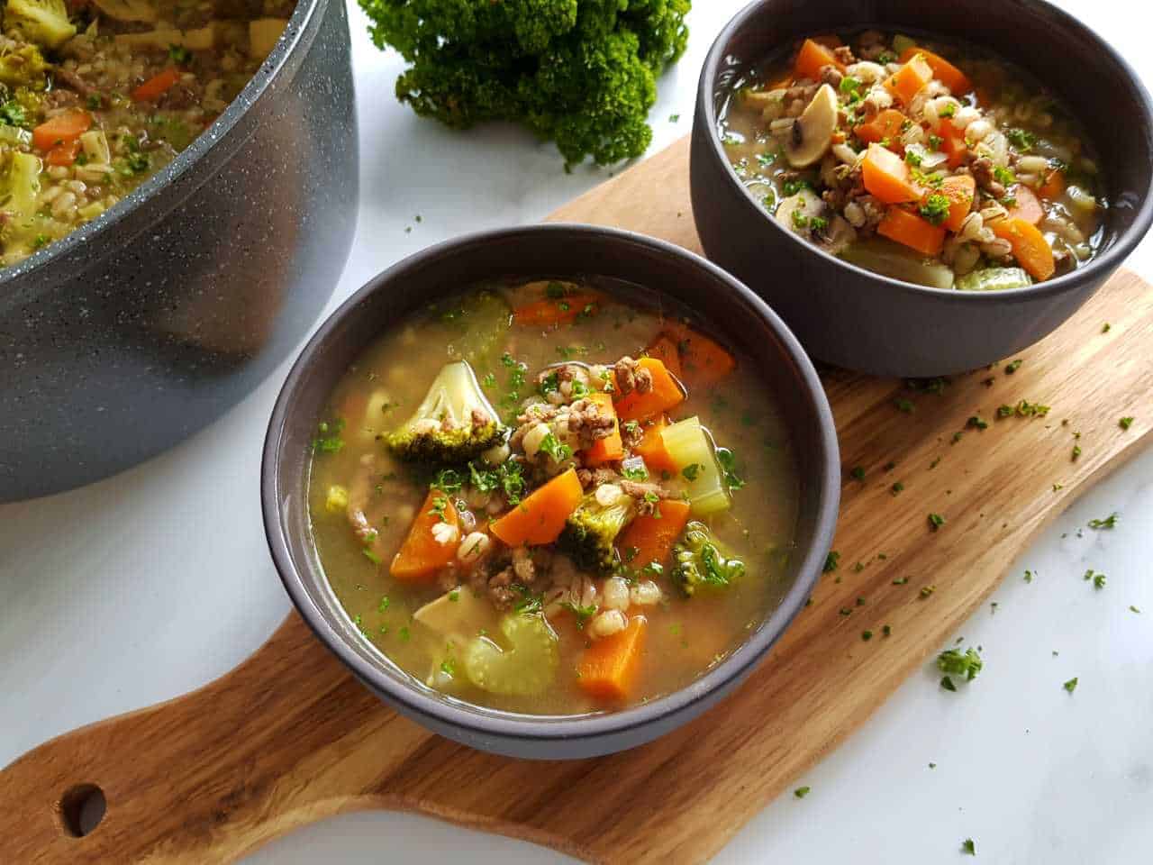 Barley soup with ground beef in bowls on a wooden chopping board.