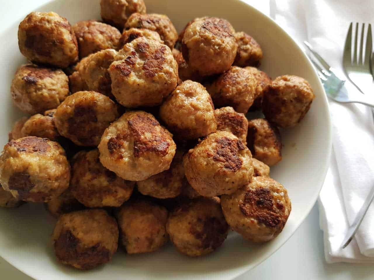 Beef and pork meatballs on a white plate next to forks.