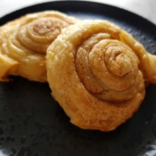 Cinnamon puff pastry rolls on a black plate.