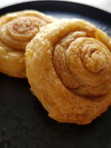 Cinnamon puff pastry rolls on a black plate.