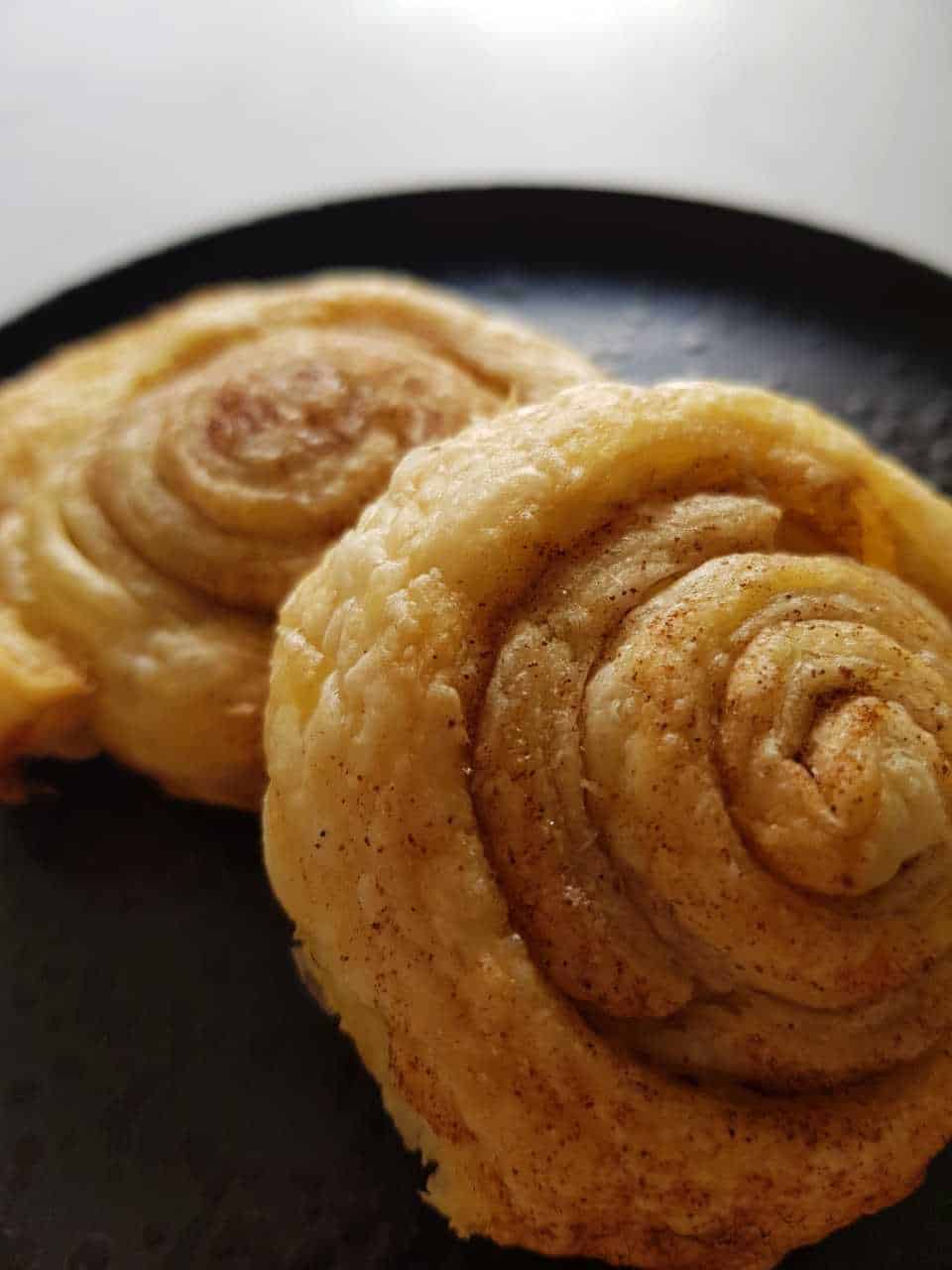 Cinnamon rolls with puff pastry on a black plate on a white table.