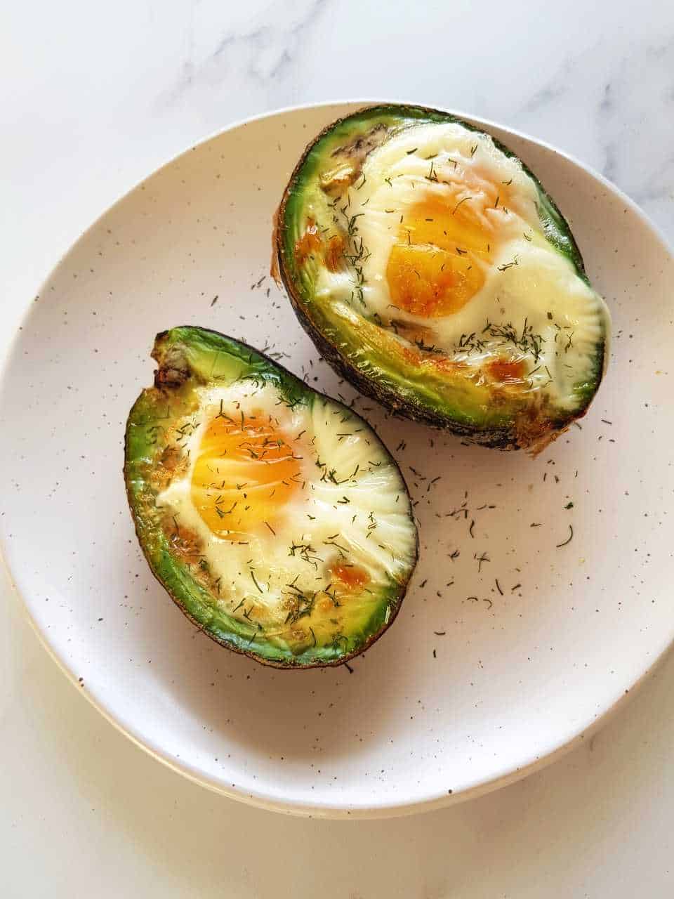 Egg baked in avocado on a white plate on a marble table.