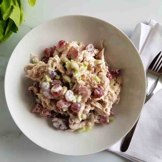 Grape and chicken salad in a white bowl on a marble table. Forks places on a white napkin on the side.