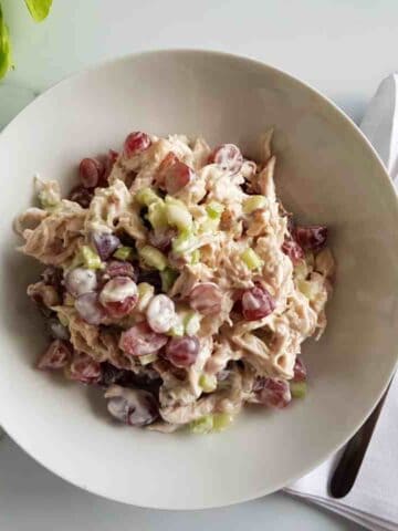 Grape and chicken salad in a white bowl on a marble table. Forks places on a white napkin on the side.