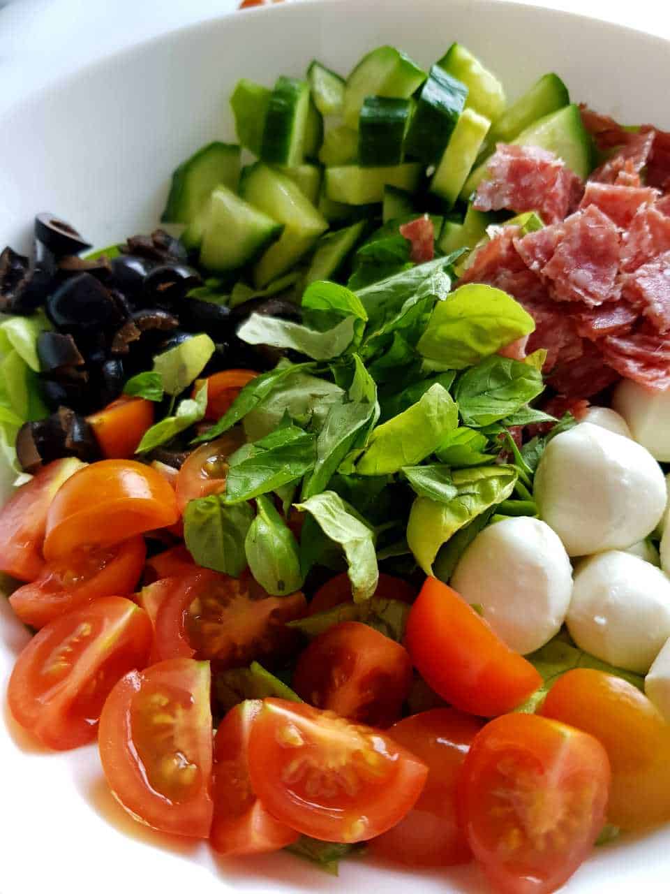 Italian salad with salami in a white bowl.