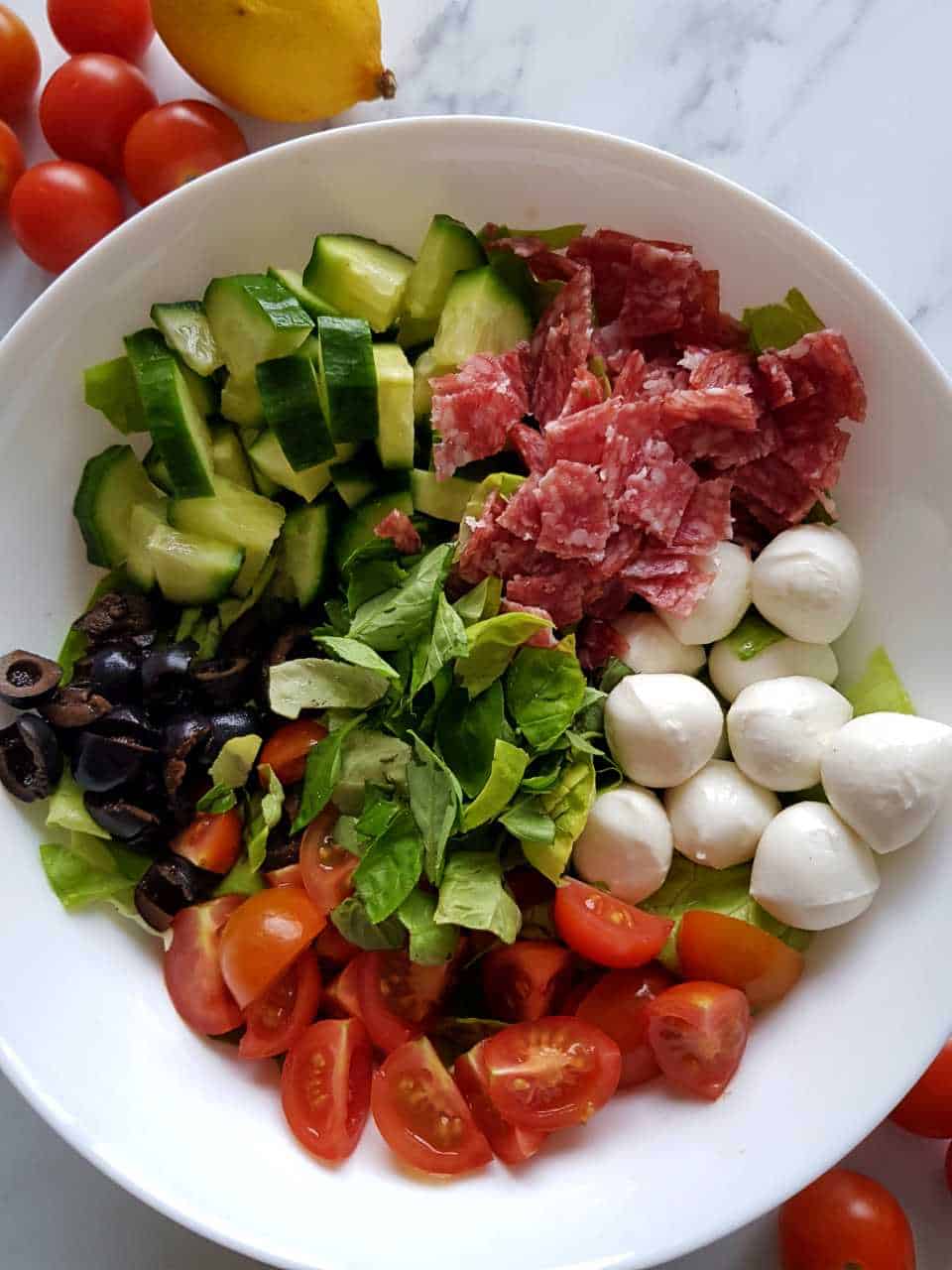 Italian salad in a white salad bowl on a marble table.