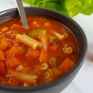 Minestrone soup in a gray bowl on a marble table.