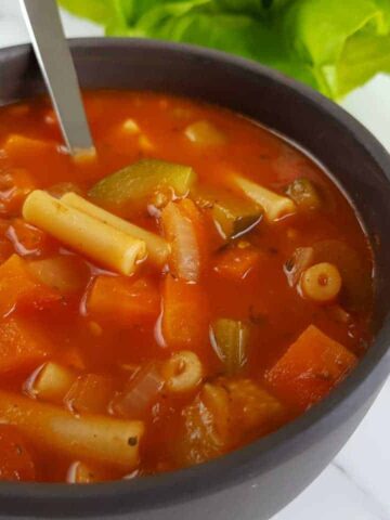 Minestrone soup in a gray bowl on a marble table.