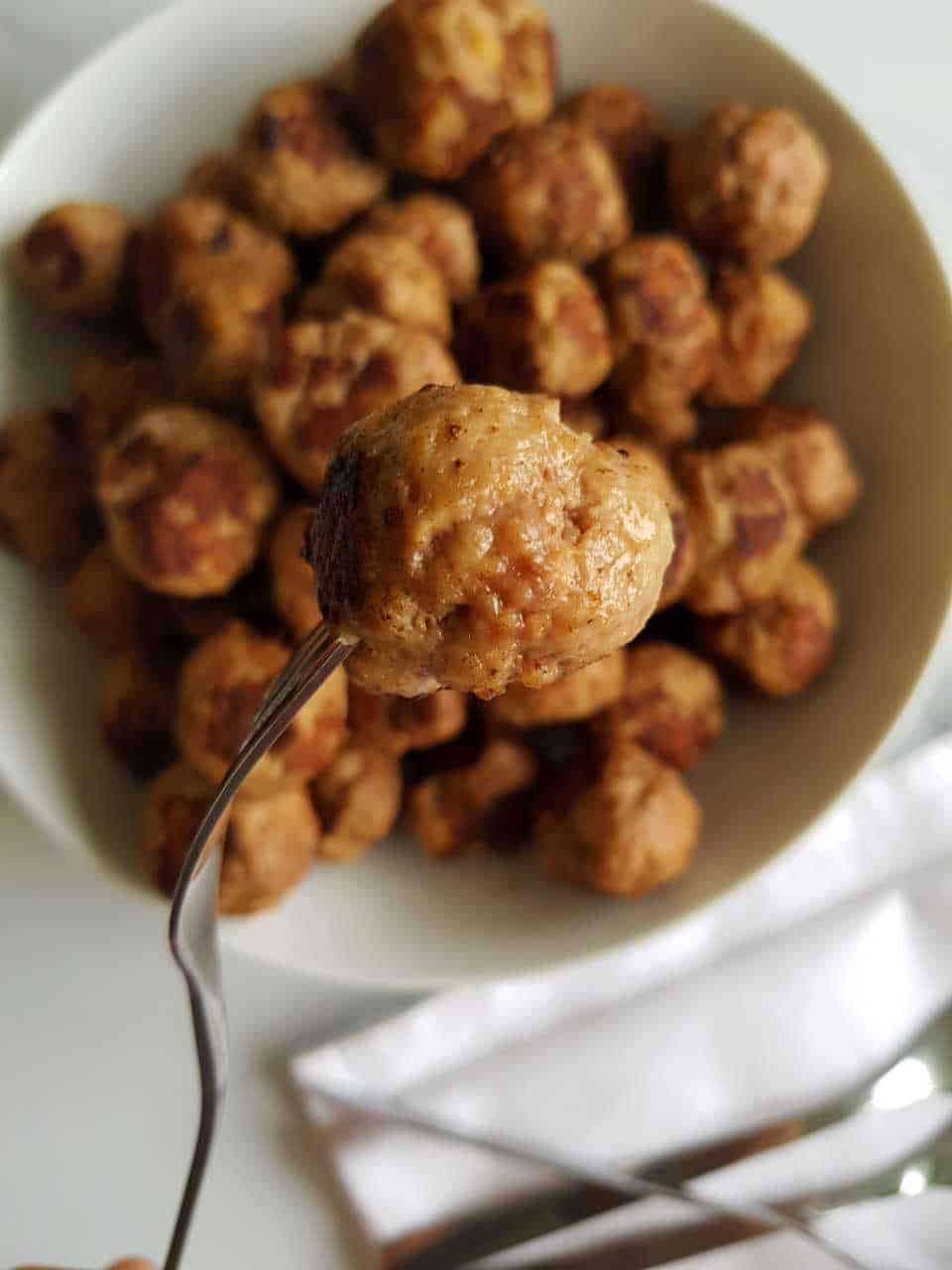 Pork and beef meatballs on a white plate. One meatballs is on a fork.