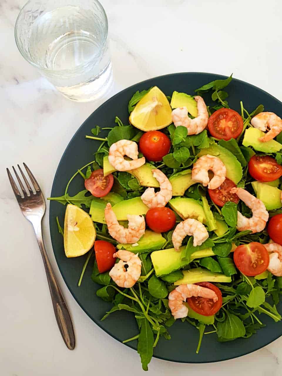 Prawn and avocado salad on a blue plate on a marble table.