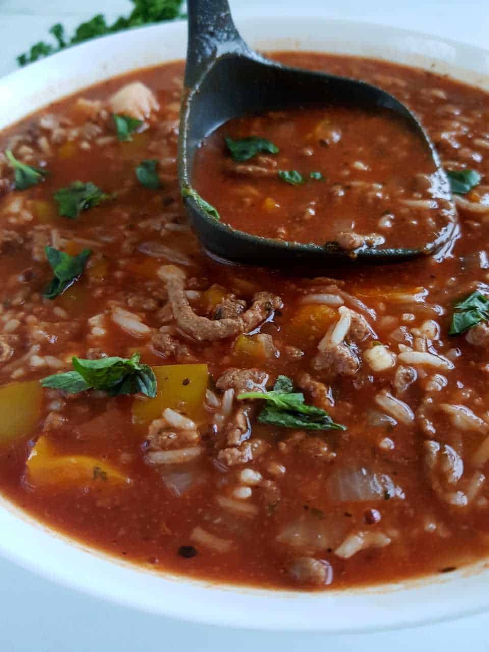 Slow cooker stuffed pepper soup in a white bowl, a ladle serving up a portion.