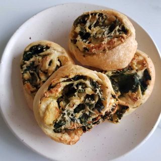 Spinach and feta pinwheels on a white plate on a marble table.