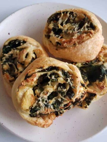 Spinach and feta pinwheels on a white plate on a marble table.