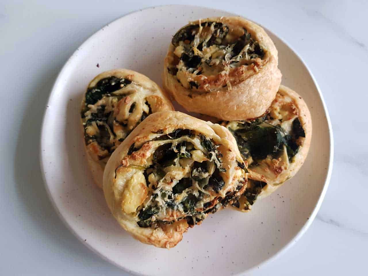 Spinach and feta pinwheels on a white plate on a marble table.