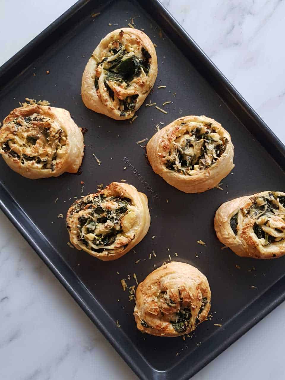 Spinach and feta puff pastry pinwheels on a baking tray on a marble table.