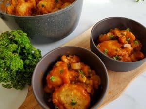 Vegetable stew with dumplings in gray bowls on a wooden chopping board.