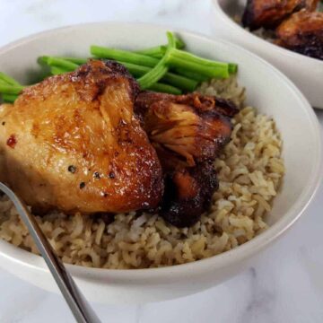 Adobo chicken in a white bowl with rice and green beans on a marble table.