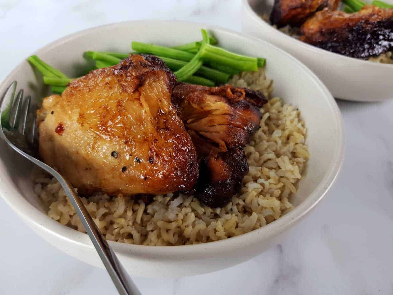 Adobo chicken in a white bowl with rice and green beans on a marble table.