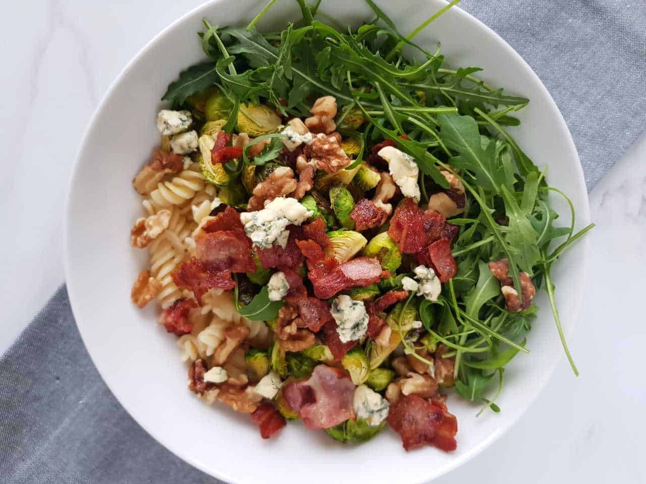 Brussels sprout salad with bacon in a white bowl on a marble table.