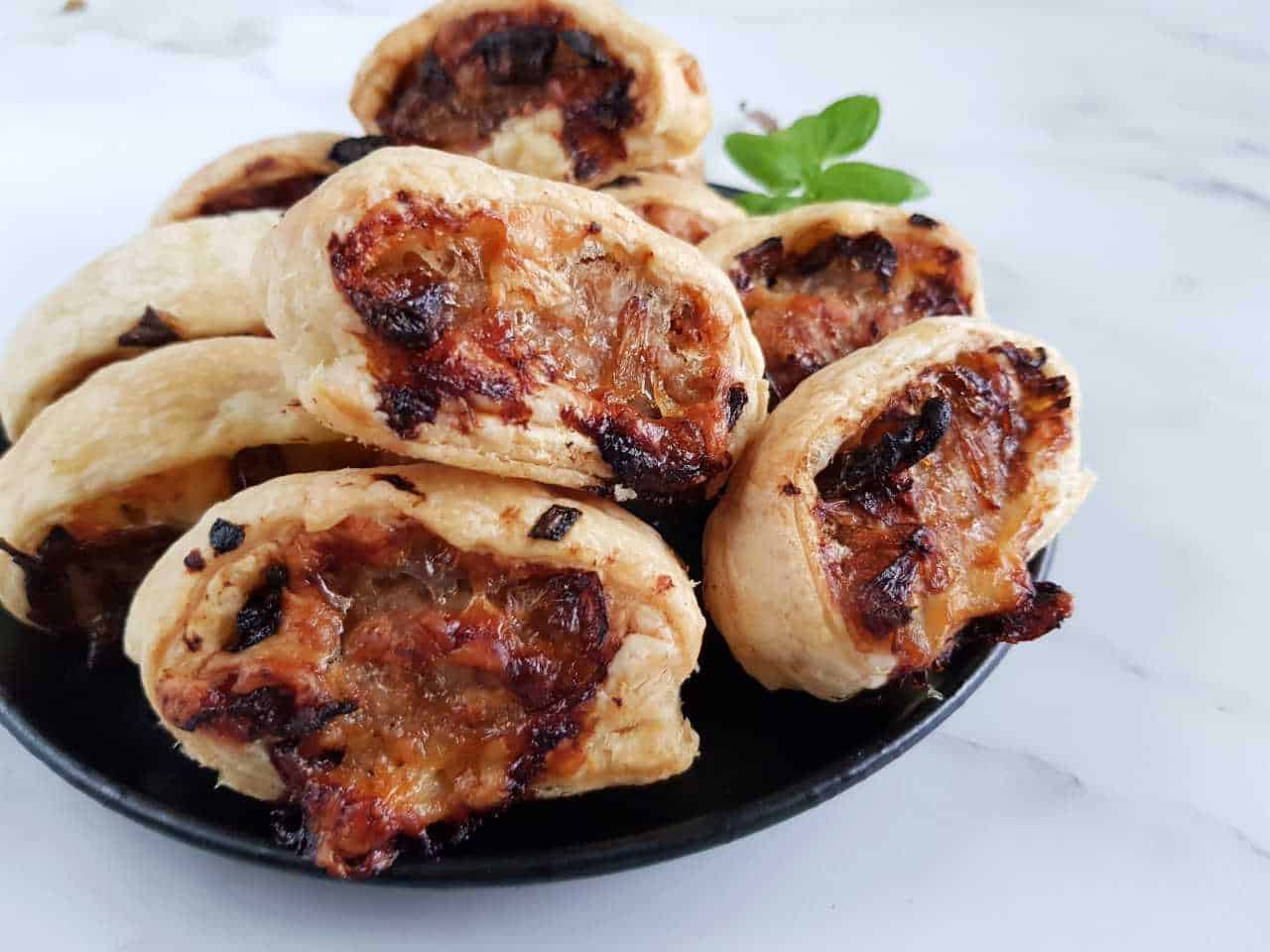 Caramelized onion and cheese sausage rolls on a black plate.