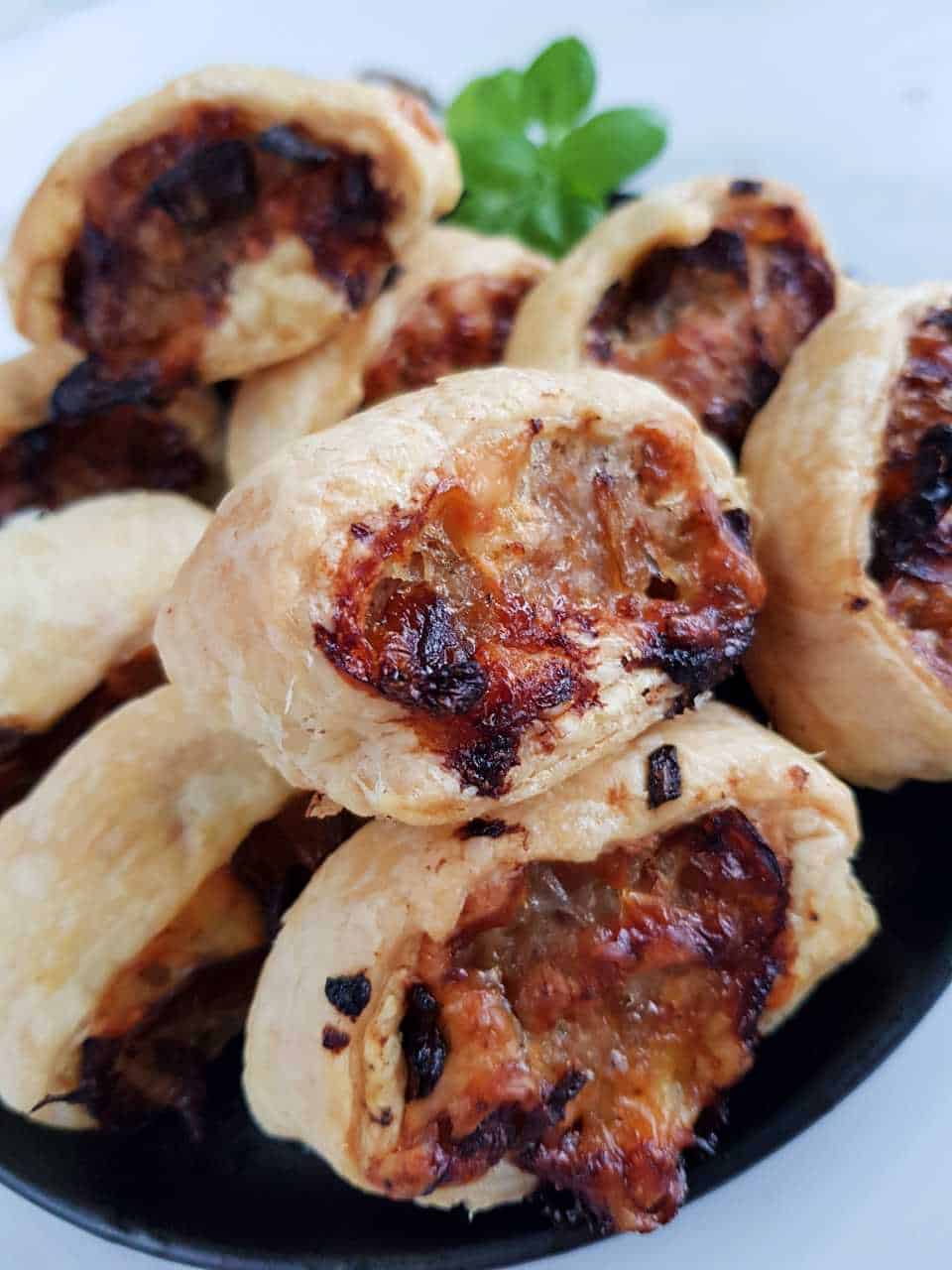 Cheese and onion sausage rolls on a black plate on a white table.