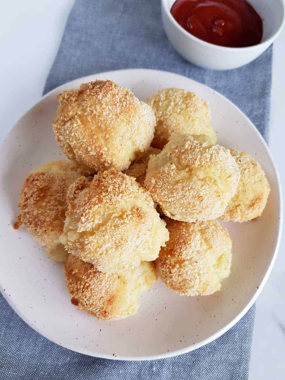 Cheese and potato balls on a white plate on a grey table cloth.