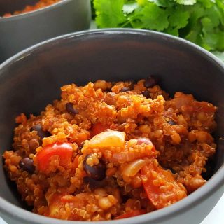 Chili with quinoa in a gray bowl with a bunch of coriander in the background.