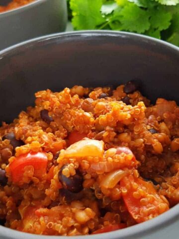 Chili with quinoa in a gray bowl with a bunch of coriander in the background.