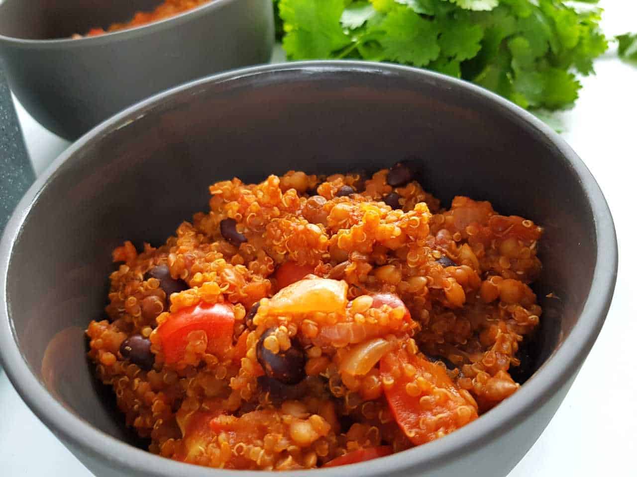 Chili with quinoa in a gray bowl with a bunch of coriander in the background.