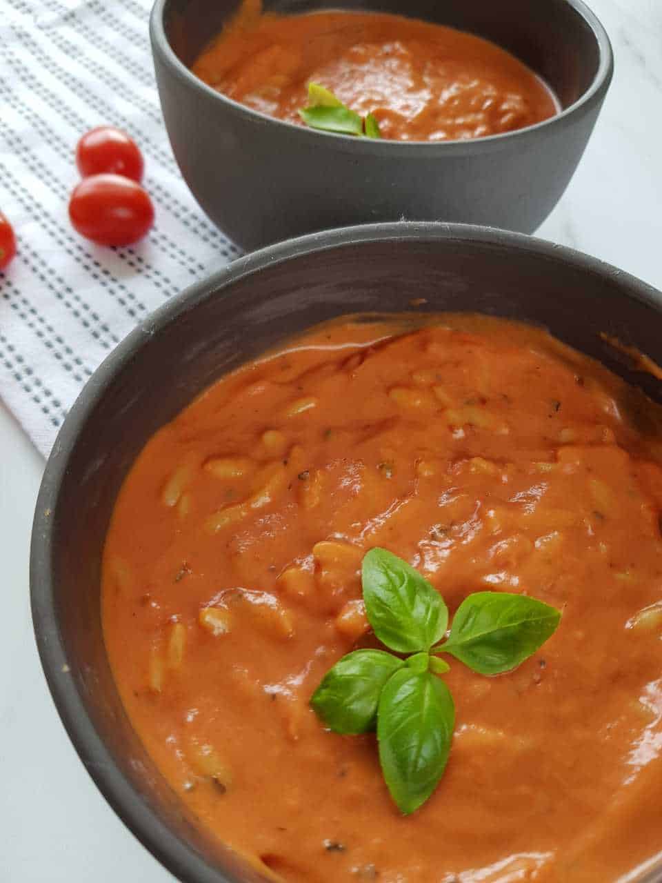 Creamy tomato orzo soup in gray bowls on a white tablecloth.