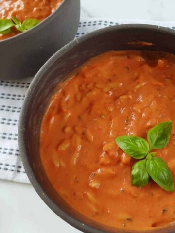 Creamy tomato soup with orzo in gray bowls on a white table with cherry tomatoes on the side.