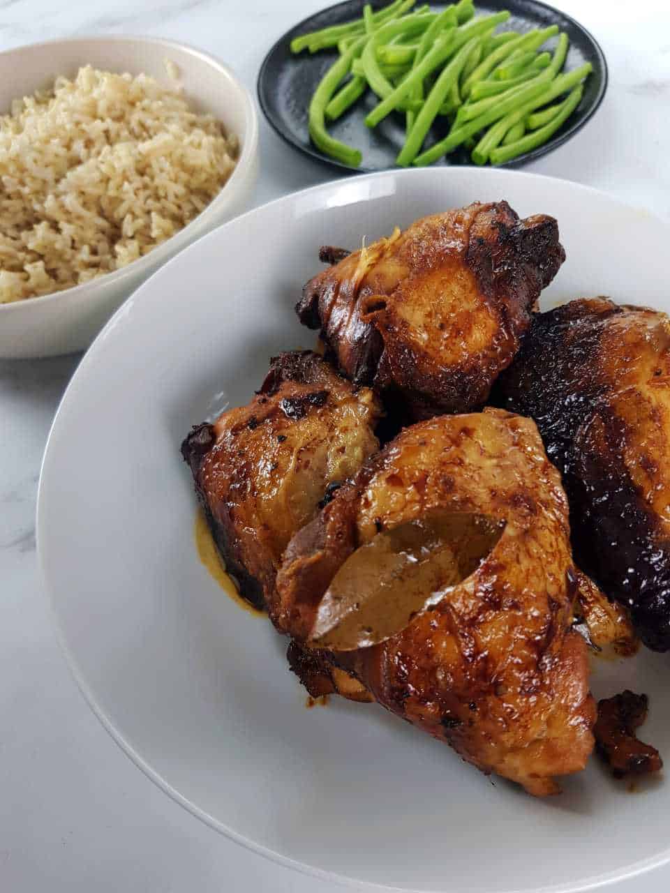 Crockpot adobo chicken in a white bowl with green beans and rice on the side.