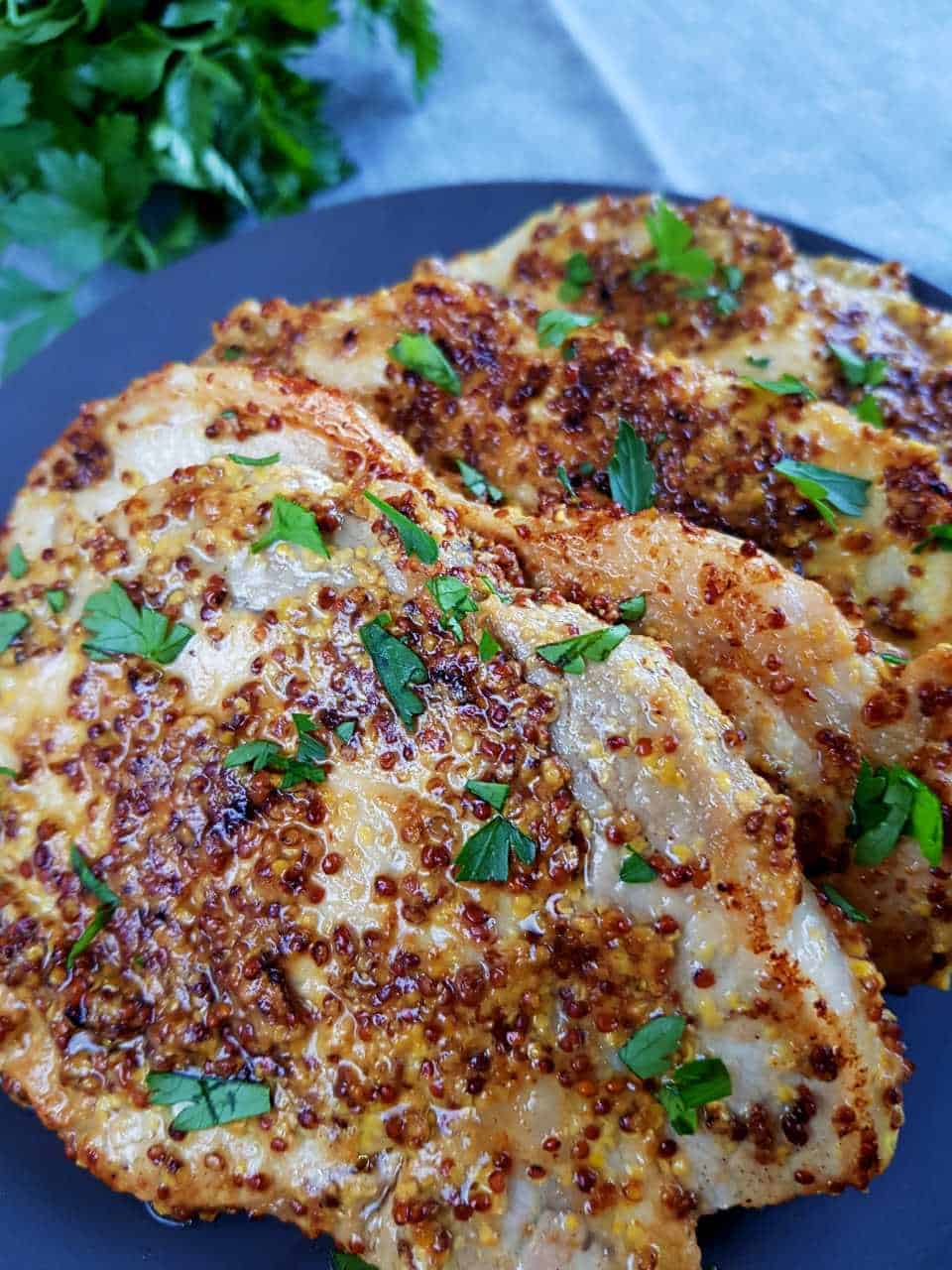 Honey mustard pork chops on a plate with herbs in the background.